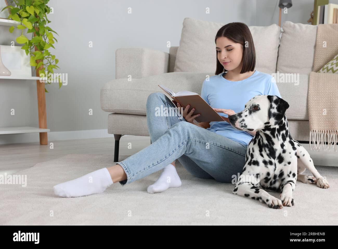 Bella giovane donna che legge un libro e il suo adorabile cane dalmata sul pavimento a casa. Adorabile animale domestico Foto Stock