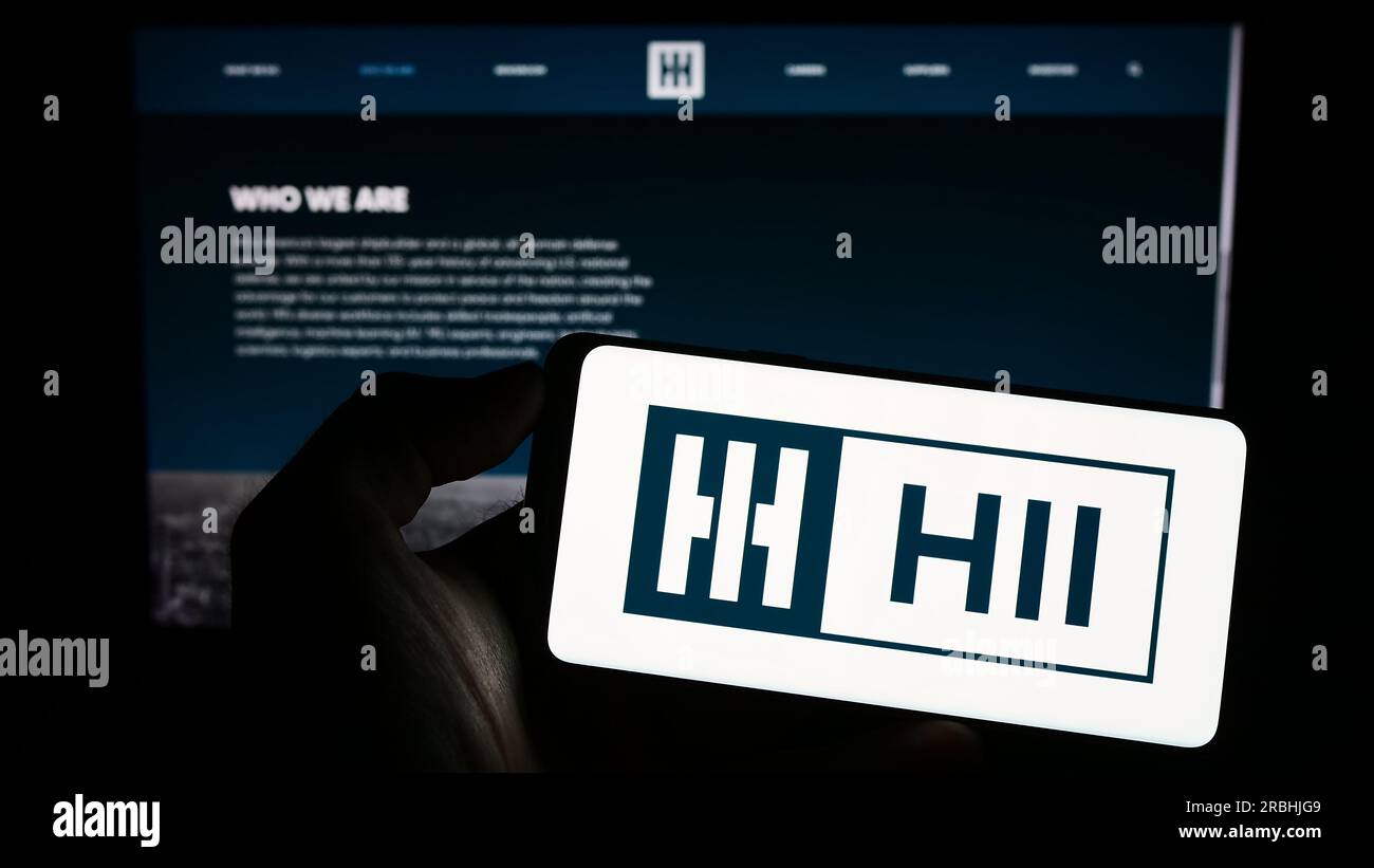 Persona che possiede uno smartphone con il logo della società di costruzione navale statunitense HII Corporate sullo schermo davanti al sito Web. Concentrarsi sul display del telefono. Foto Stock