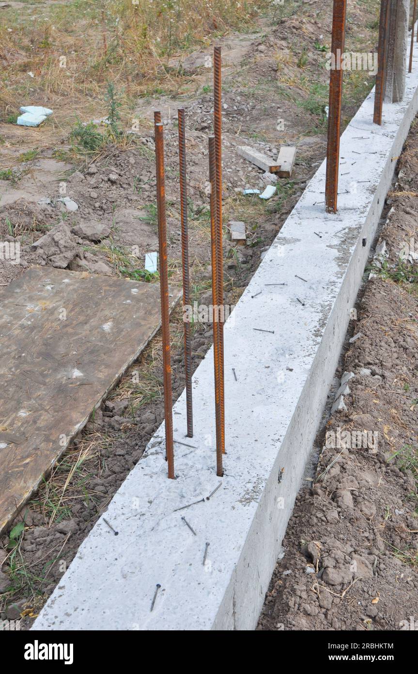 Il piè di pagina in calcestruzzo per il montaggio di una nuova recinzione. Fondazioni di recinzione. Primo piano sulla base in cemento armato per la fondazione di recinzioni con barra di rinforzo. Foto Stock