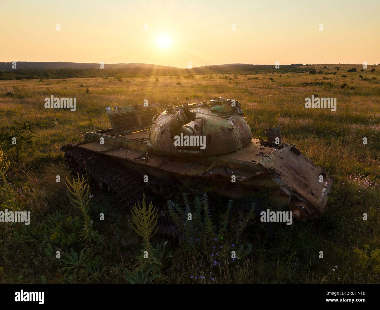 Distrutto arrugginito, abbandonato e bruciato carro armato nei campi verdi al tramonto. Puoi usare questa immagine come illustrazione, ad esempio la guerra Foto Stock