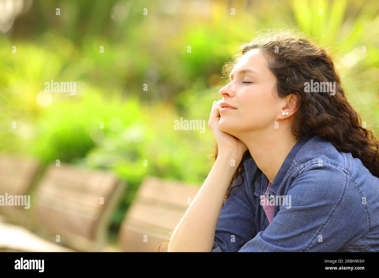 Donna che rilassa la mente chiudendo gli occhi seduti su una panchina in un parco Foto Stock