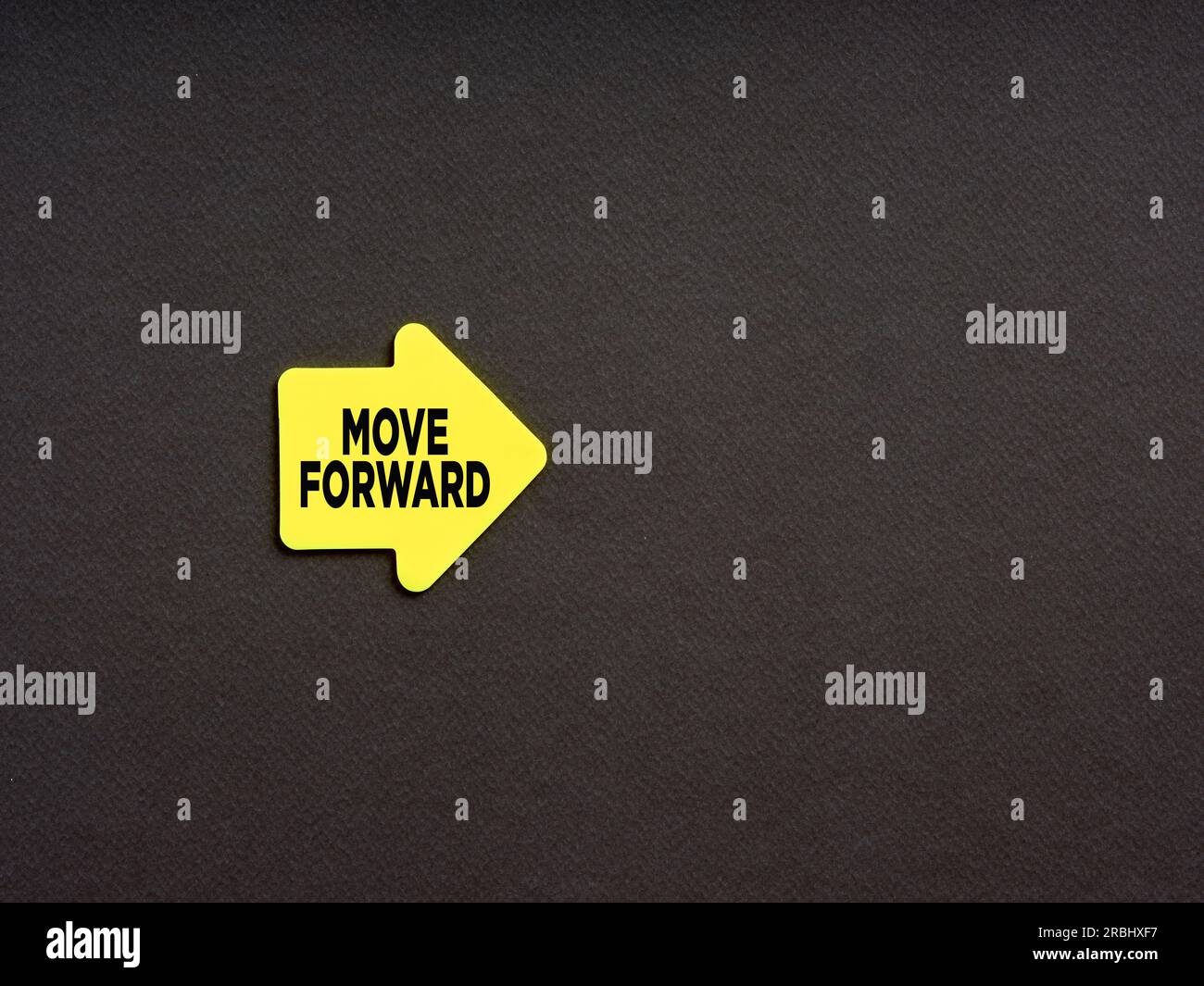 Concetto motivazionale per il miglioramento dell'azienda o della carriera. Adesivo giallo a forma di freccia con la parola "muoversi in avanti" su sfondo nero. Foto Stock