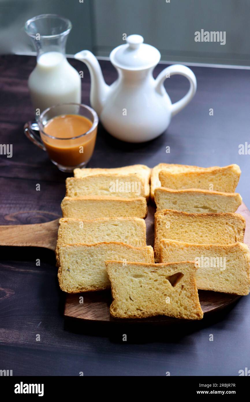 Tè Time snack. Salutare rusk di grano servito con tè di masala caldo indiano e brocca di latte su sfondo nero. Conosciuto anche come Mumbai cutting chai. Foto Stock