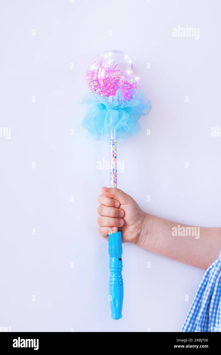 Bacchetta magica blu brillante nelle mani di una ragazza in abito a quadri su sfondo chiaro senza volto con spazio per la copia. Fai avverare desideri e sogni. Sorpreso e.. Foto Stock