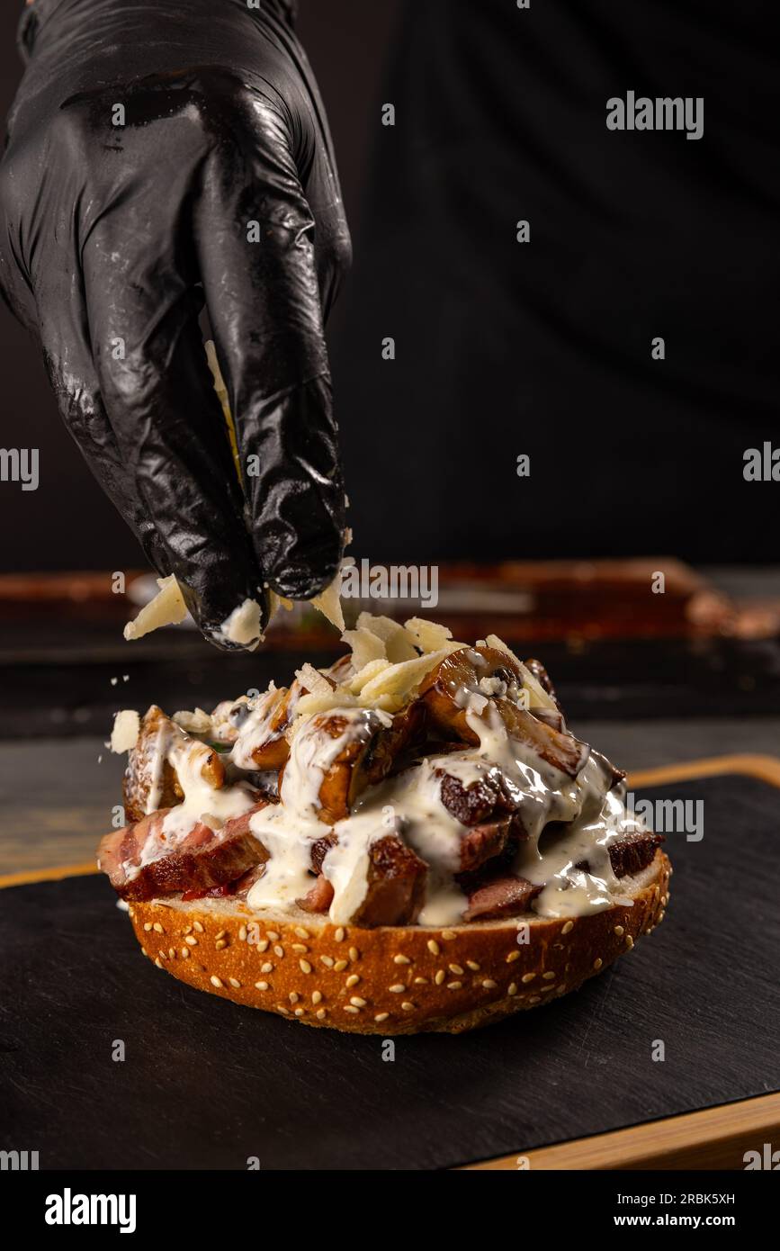 Lo chef prepara un hamburger di bistecca su un tavolo con l'aggiunta di formaggio grattugiato Foto Stock