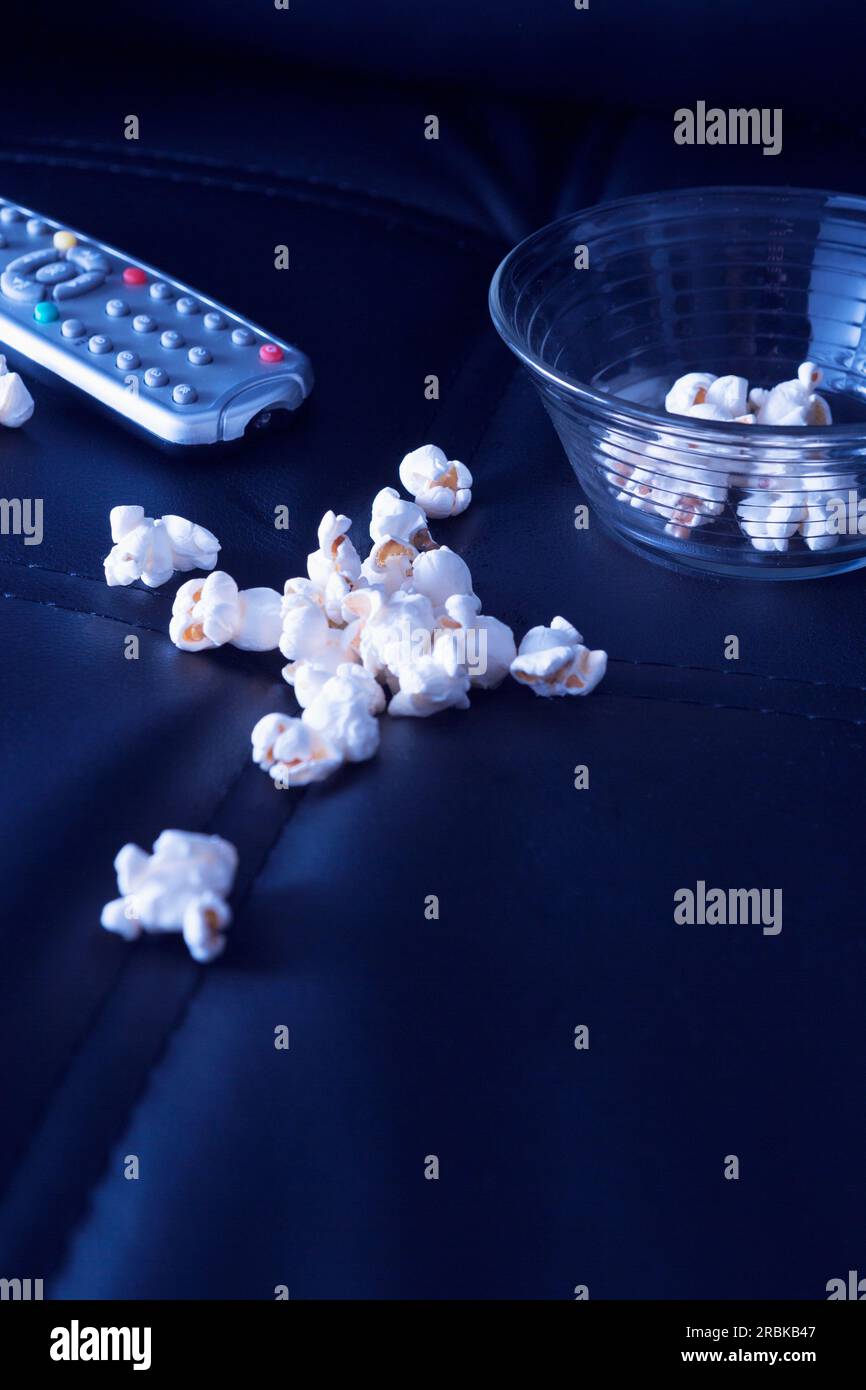 Popcorn e telecomando sul divano nero la sera Foto Stock