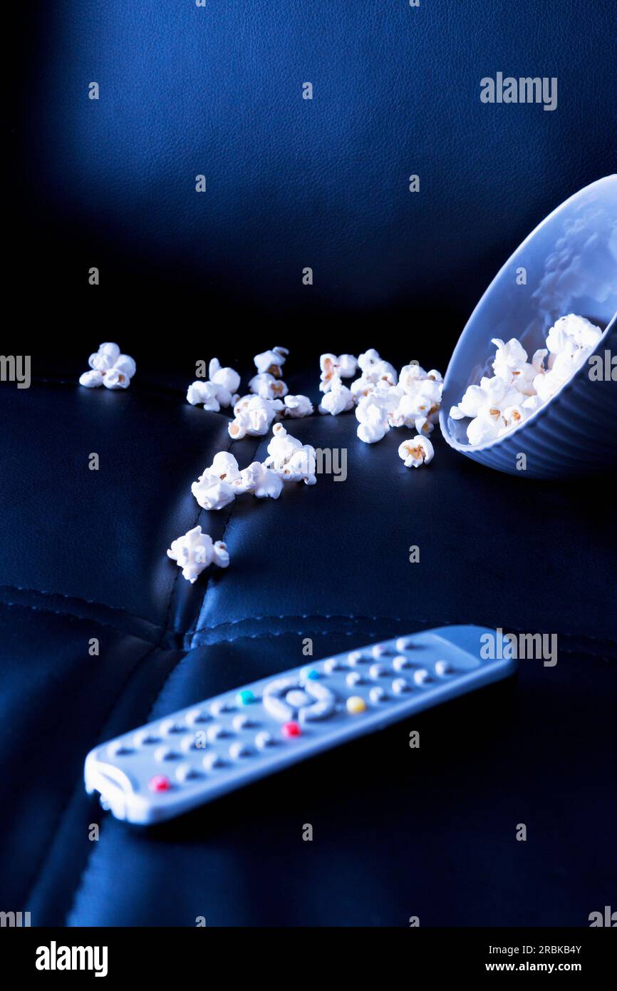 Ciotola di popcorn e telecomando sul divano nero la sera Foto Stock