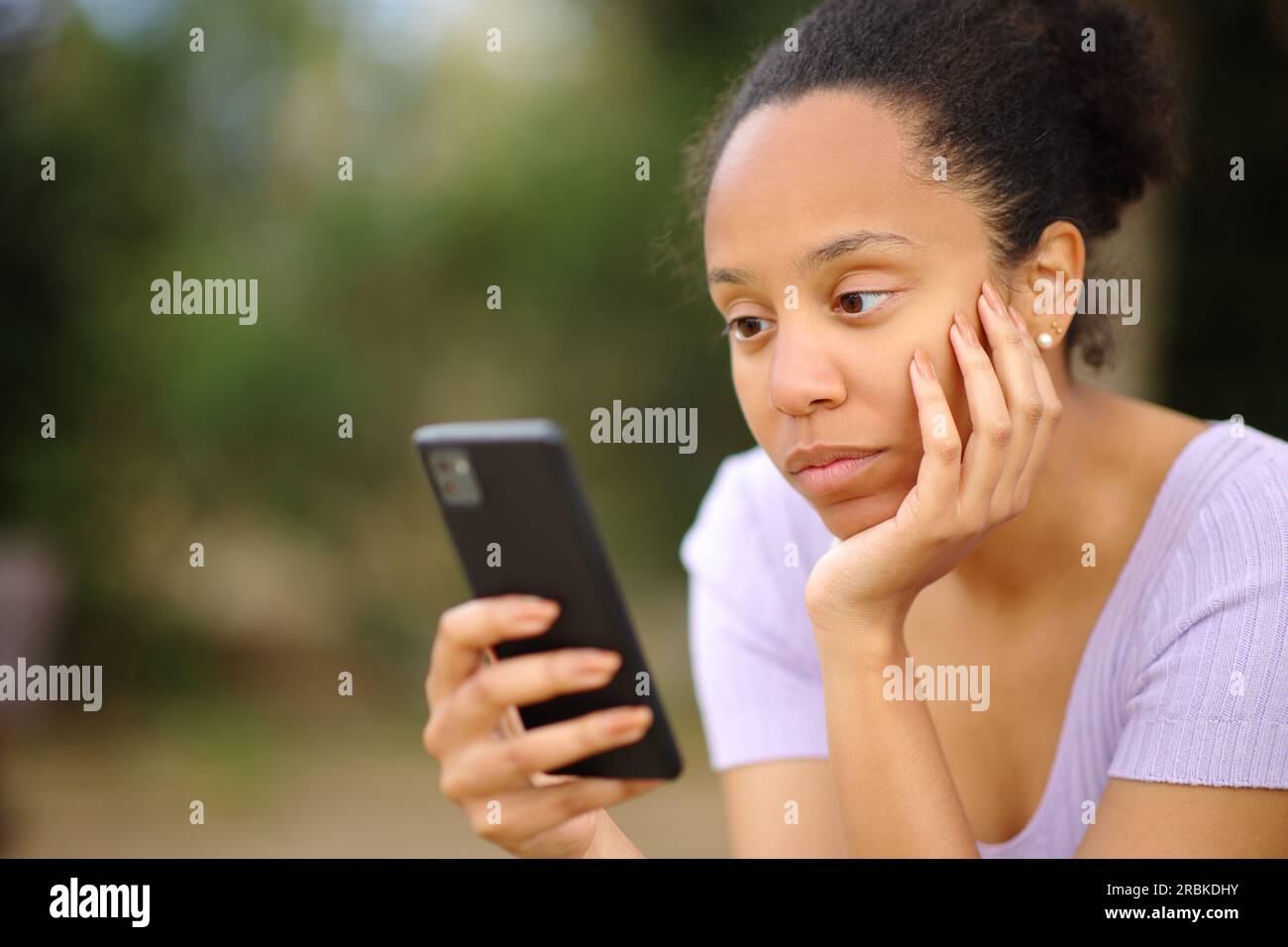 Una donna nera seria che usa il cellulare seduto in un parco Foto Stock