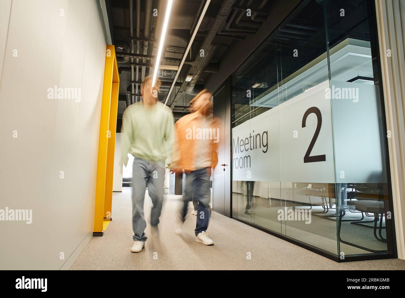 lunga esposizione di due partner commerciali di successo che camminano lungo la sala riunioni nel corridoio di un ufficio contemporaneo con un ambiente di coworking e un'alta Foto Stock