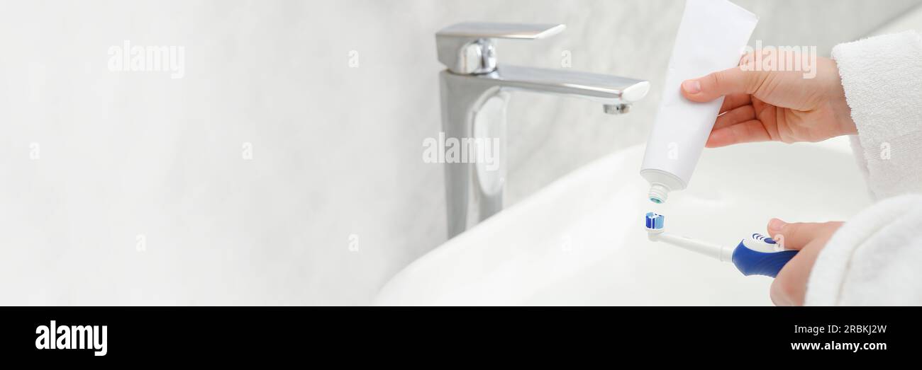 Donna che strizza dentifricio dal tubo allo spazzolino elettrico sopra il  lavandino in bagno, primo piano. Design banner con spazio per il testo Foto  stock - Alamy