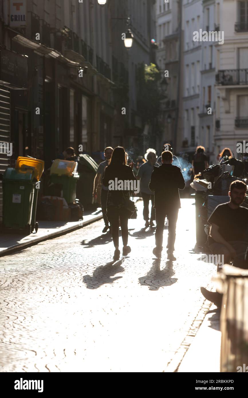 Due persone che fumano con silhouette camminano verso il tramonto nel centro di Parigi. Foto Stock