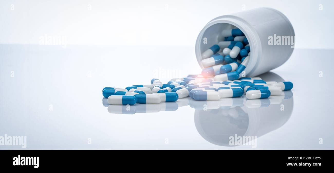 Pillole di capsule antibiotiche blu-bianche sparse dai flaconi di plastica. Resistenza agli antibiotici. Farmaci prescritti. Sanità e medicina. Foto Stock