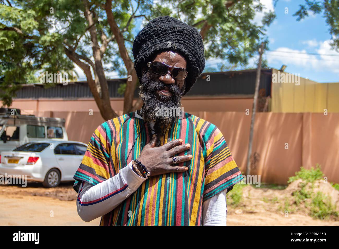 Felice Rastafari che indossa abiti colorati e cappello di lana, con dreadlock e un modo di pensare positivo, anello di pace al dito Foto Stock