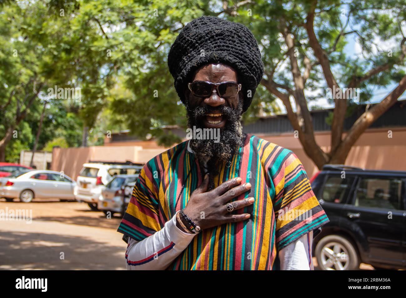 Felice Rastafari che indossa abiti colorati e cappello di lana, con dreadlock e un modo di pensare positivo, anello di pace al dito Foto Stock