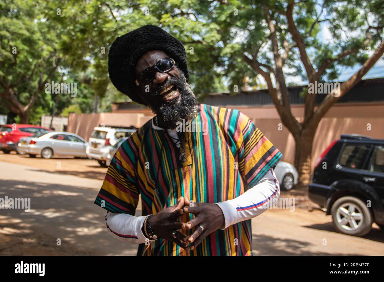 Felice Rastafari che indossa abiti colorati e cappello di lana, con dreadlock e un modo di pensare positivo, anello di pace al dito Foto Stock