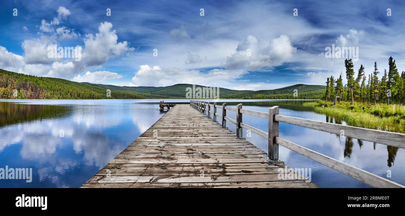 Bellissimo lago di montagna con riflessi e molo in legno. Soffici nuvole bianche e cielo blu riflessi in acqua ferma Foto Stock