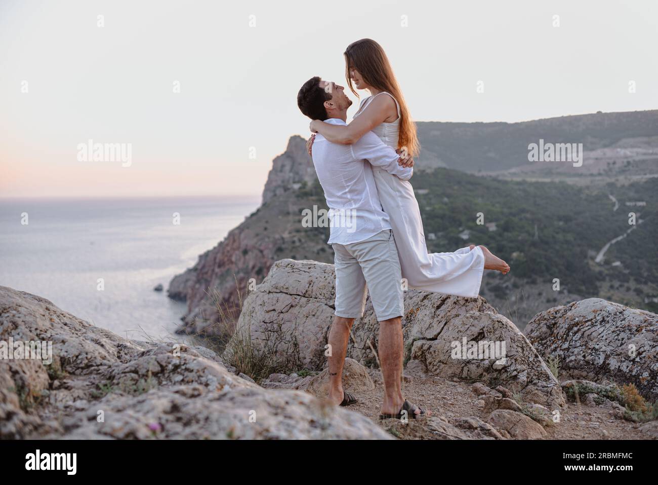 Bella giovane e amorevole coppia uomo dall'aspetto mediorientale e una donna caucasica abbracciano, baciano all'alba. Storia d'amore all'aperto. Foto Stock