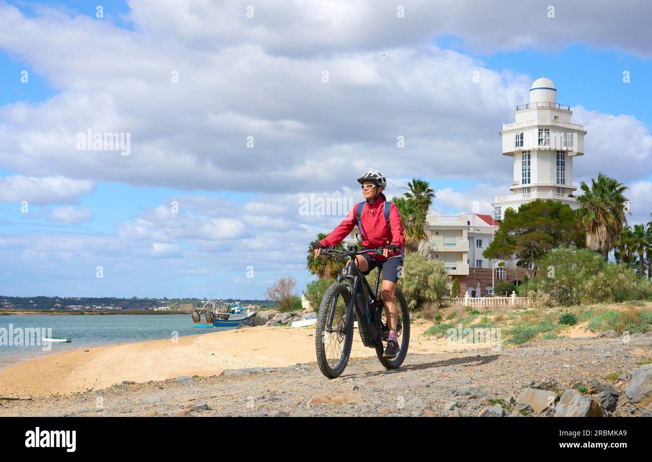 Bella donna anziana che pedala con la sua mountain bike elettrica su una via verde nelle zone umide di Isla Christina, Andalusia, Spagna Foto Stock