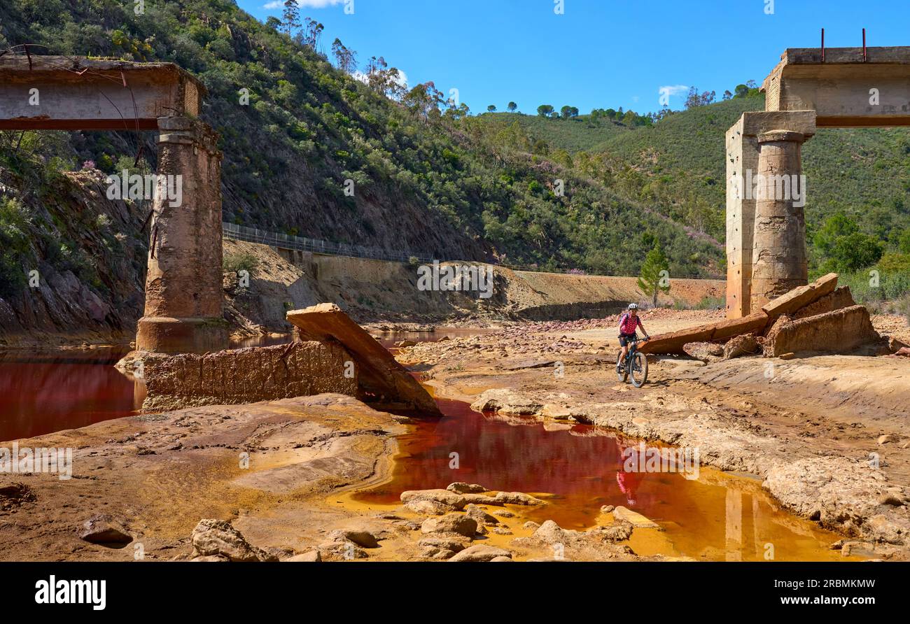 Una donna simpatica in bici elettrica in un tour in bicicletta lungo il fiume Rio Tinto con le sue acque rosse naturali in Andalusia, Spagna Foto Stock