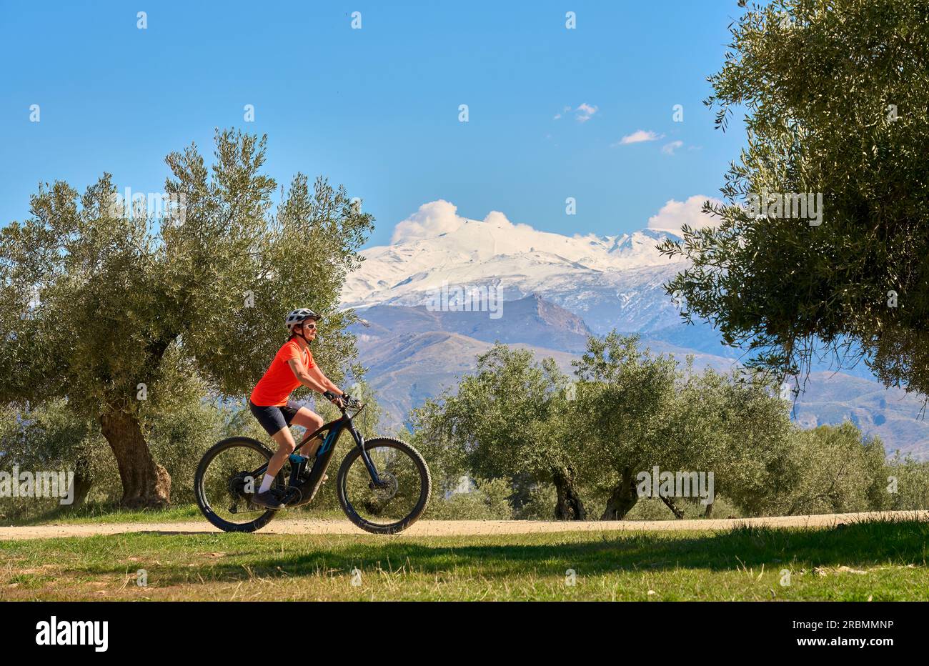 Bella donna anziana attiva che va in bicicletta con la sua mountain bike elettrica sotto le montagne innevate della Sierra Nevada spagnola, vicino a Granada, Andalus Foto Stock