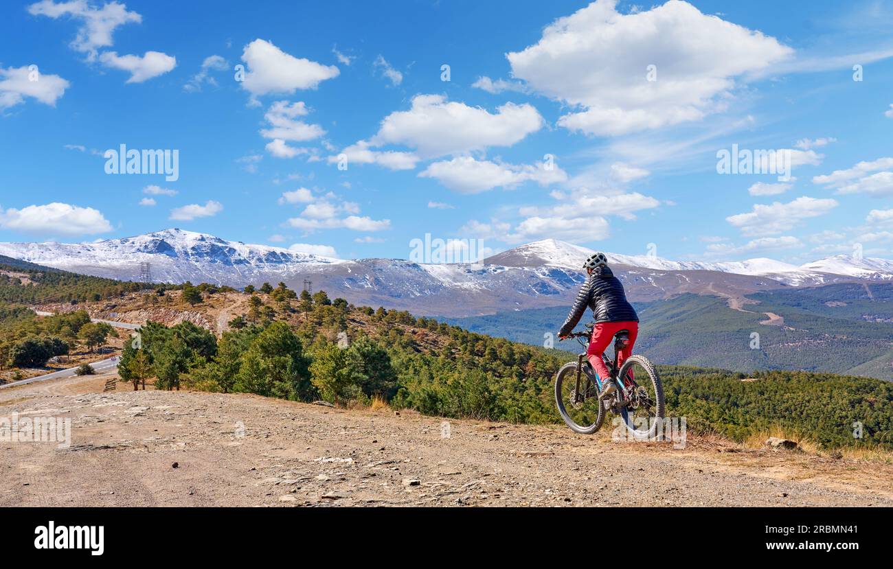 Bella donna anziana attiva che va in bicicletta con la sua mountain bike elettrica sotto le montagne innevate della Sierra Nevada spagnola, vicino a Granada, Andalus Foto Stock