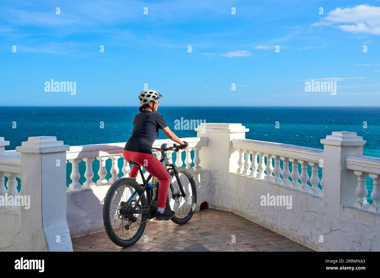 Una bella donna anziana in bicicletta con la sua mountain bike elettrica sulla costa della Costa Blanca vicino a Nerja, Andalusia, Spagna Foto Stock