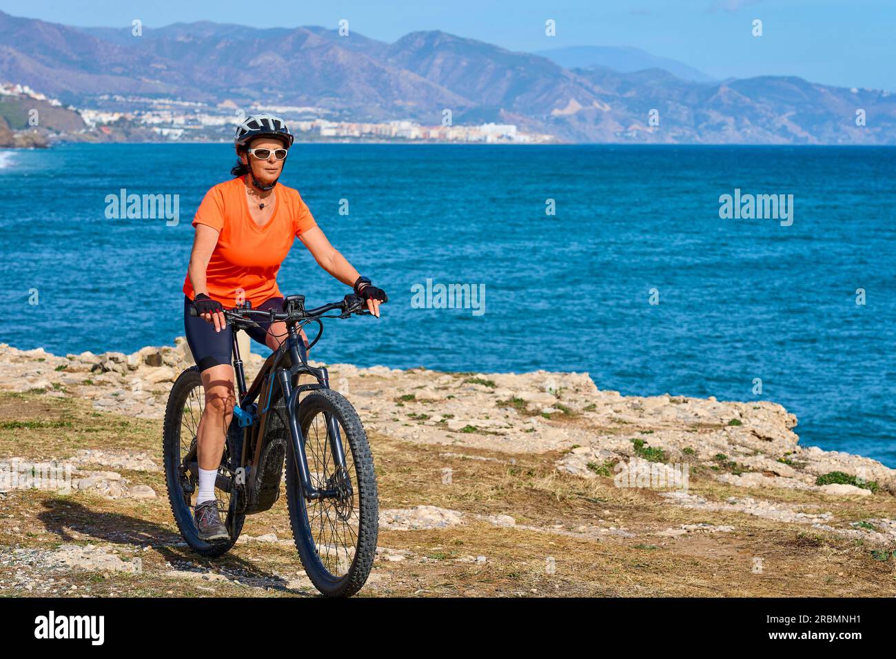 Una bella donna anziana in bicicletta con la sua mountain bike elettrica sulla costa della Costa Blanca vicino a Nerja, Andalusia, Spagna Foto Stock