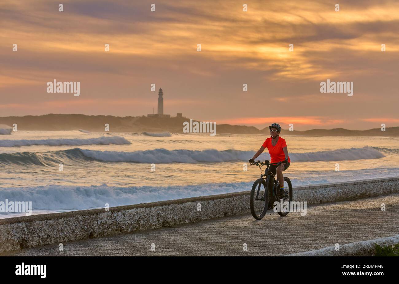 Donna attiva in bicicletta al tramonto con la sua mountain bike elettrica sulla spiaggia di Capo Trafalgar, Costa de la Luz, Andalusia, Spagna Foto Stock