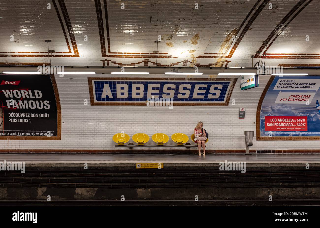 La donna controlla il cellulare mentre aspetta il treno alla stazione della metropolitana di Abbesses, linea 12, Montmartre, 18 Arr. Parigi Foto Stock