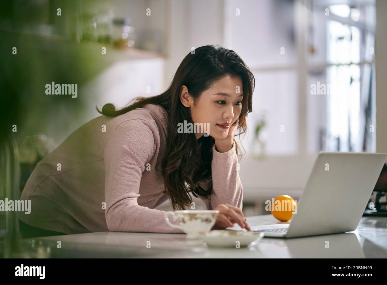 giovane donna d'affari asiatica che lavora in cucina a casa utilizzando un computer portatile Foto Stock