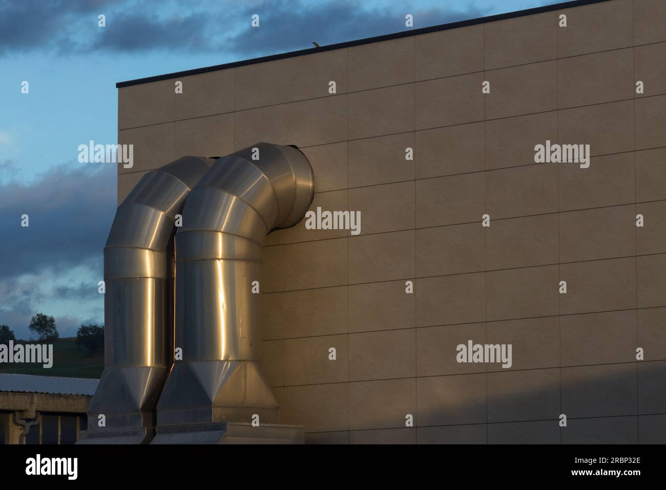 Un edificio industriale con condotti esterni visibili in un cielo serale Foto Stock