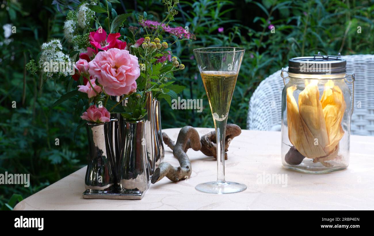 Atmosfera estiva in giardino con un bicchiere di vino, fiori e una lampada solare. Garden Sanctuary. Foto Stock