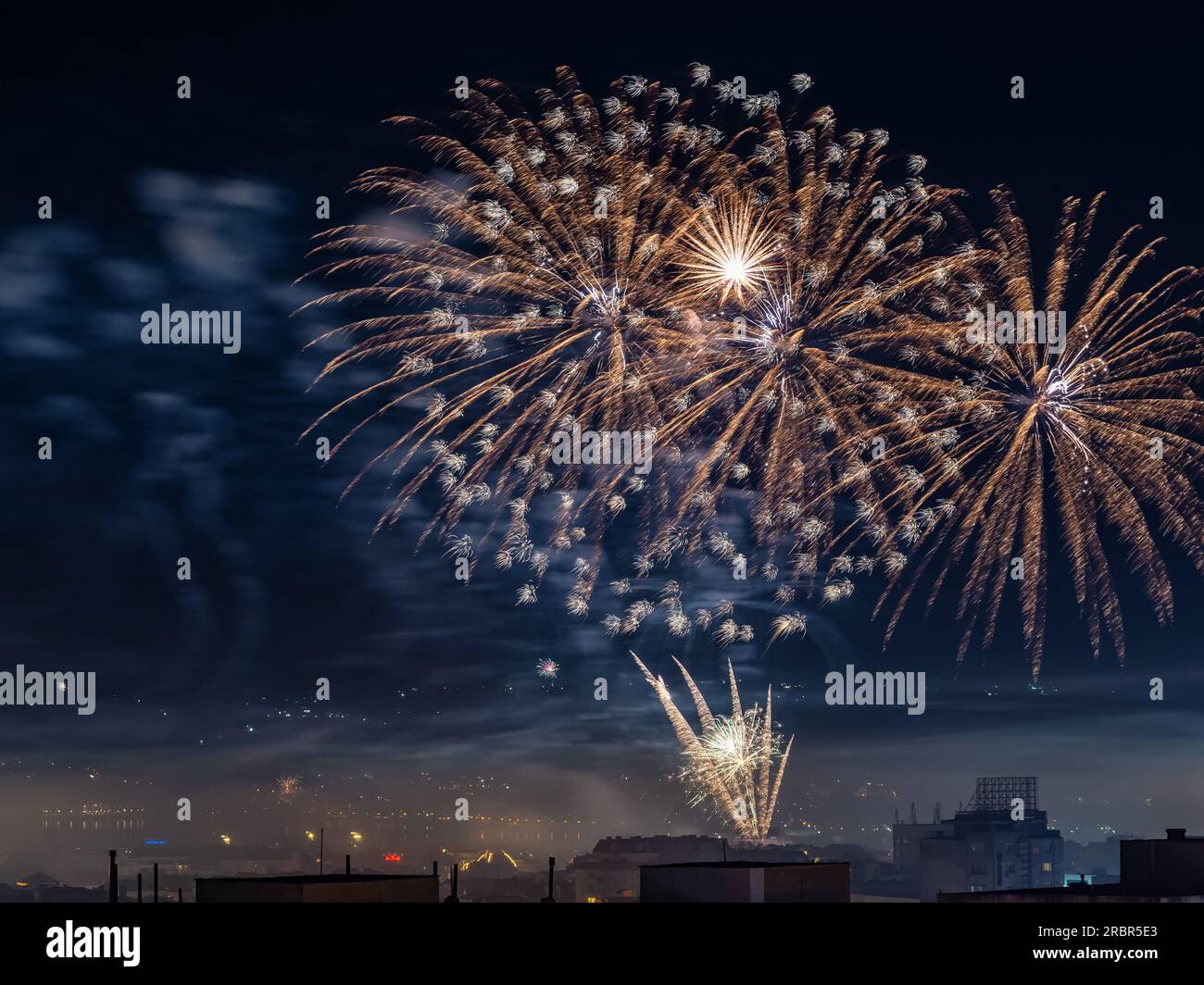Fuochi d'artificio arancioni nel cielo notturno. Spettacolo di fuochi d'artificio durante le feste in città a mezzanotte. Concetto di pirotecnico e firecrackers Foto Stock