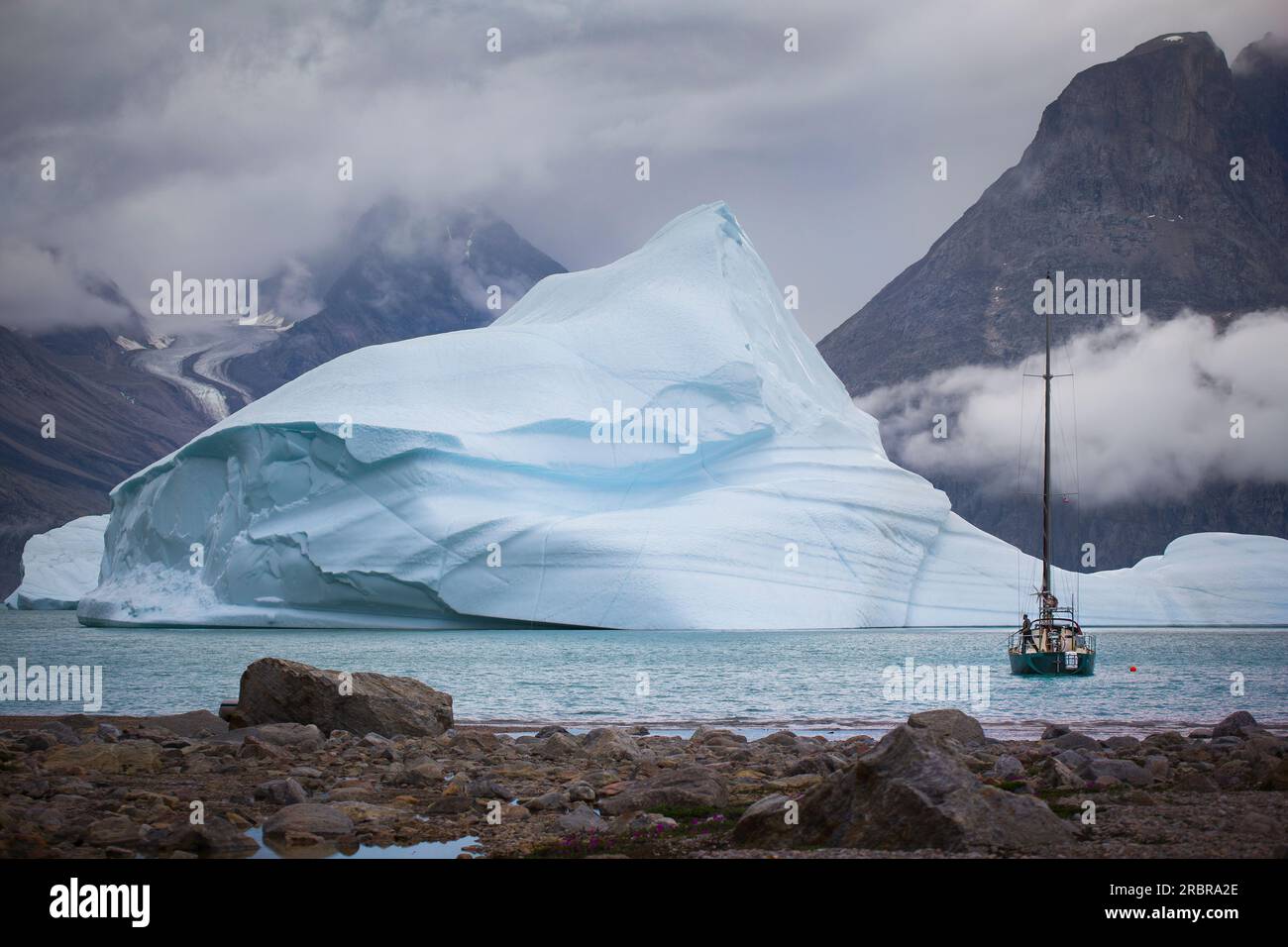 Barca a vela ancorata in un fiordo in Groenlandia. Circondato da iceberg. splendide montagne e ghiacciai sullo sfondo. L'uomo sta pescando dalla barca. Foto Stock
