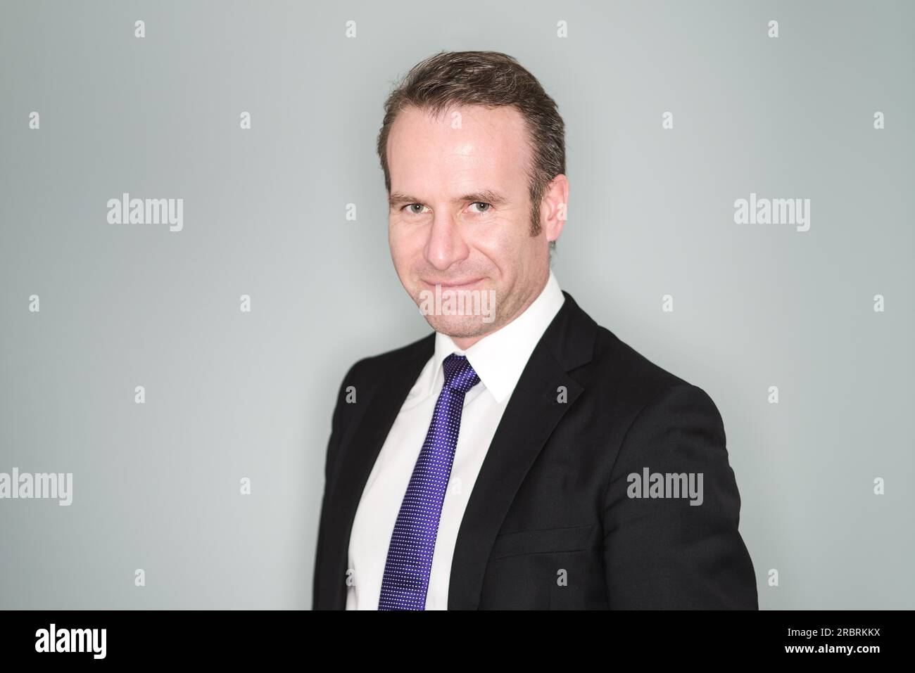 Sorridente e sicuro, bello dirigente d'affari di mezza età o uomo d'affari in un elegante vestito, un ritratto della testa e delle spalle su uno studio grigio Foto Stock