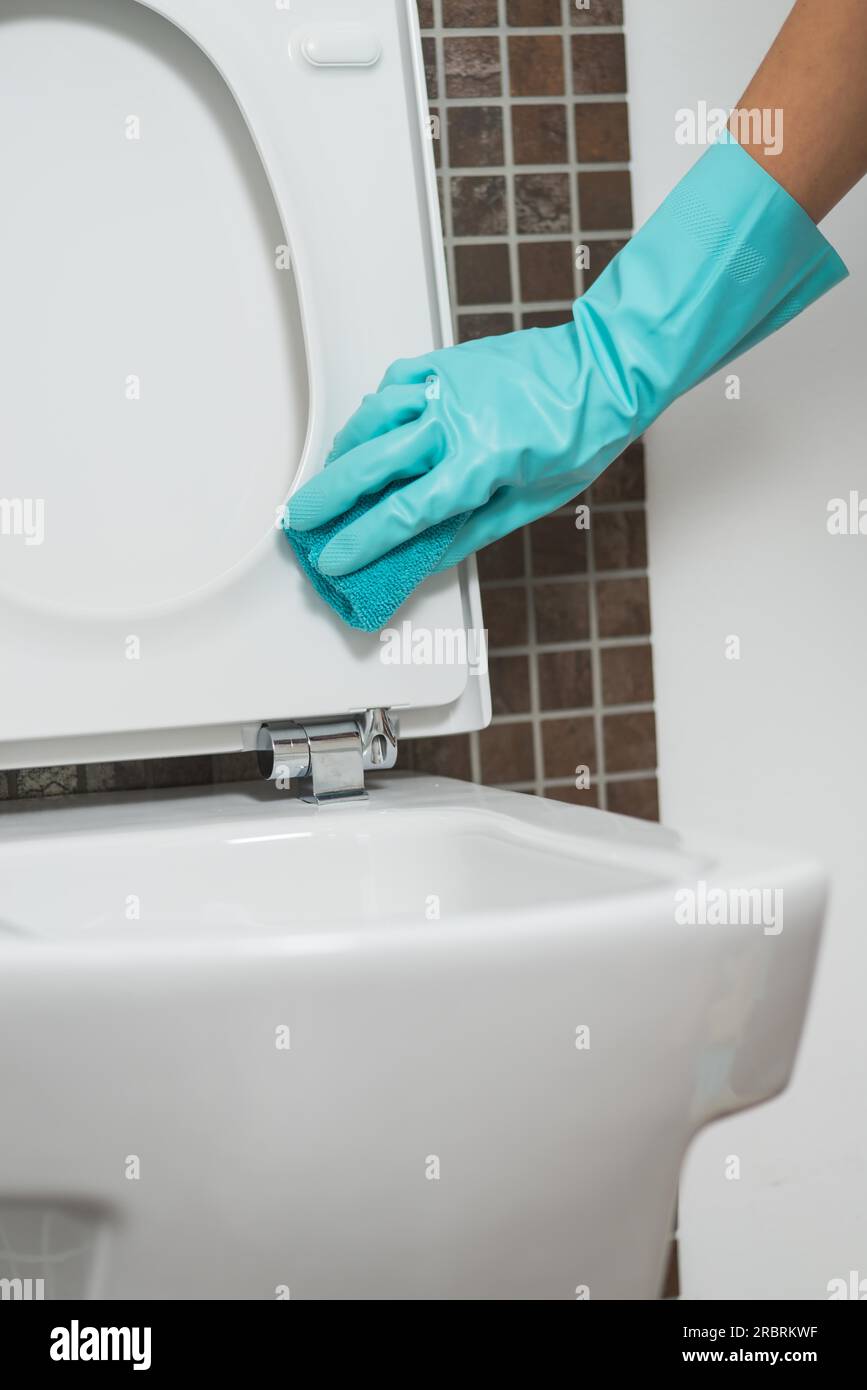 Mano di una persona che pulisce il sedile del WC con guanti di gomma con una spugna disinfettando il lato inferiore per germi e batteri durante l'esecuzione della famiglia Foto Stock