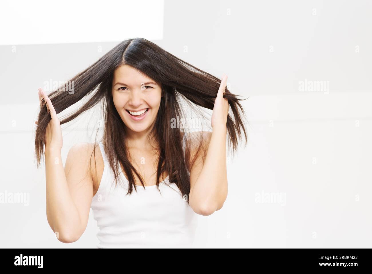 Bella e gioiosa giovane donna che gioca con i suoi lunghi capelli bruna che le fa passare le dita attraverso le trappole mentre le solleva dalla testa Foto Stock