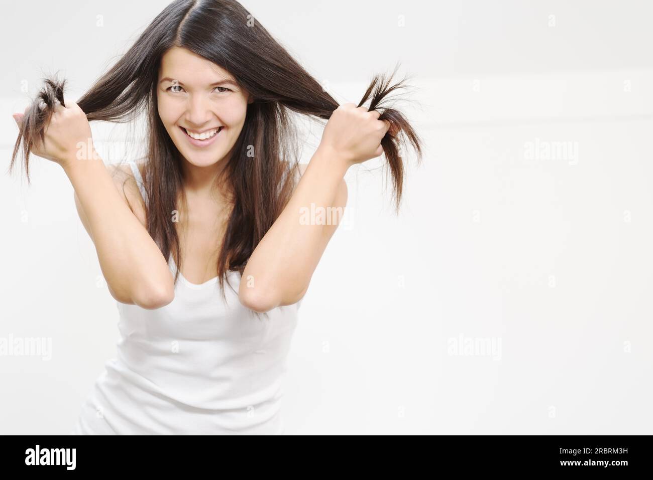Bella e gioiosa giovane donna che gioca con i suoi lunghi capelli bruna che le fa passare le dita attraverso le trappole mentre le solleva dalla testa Foto Stock