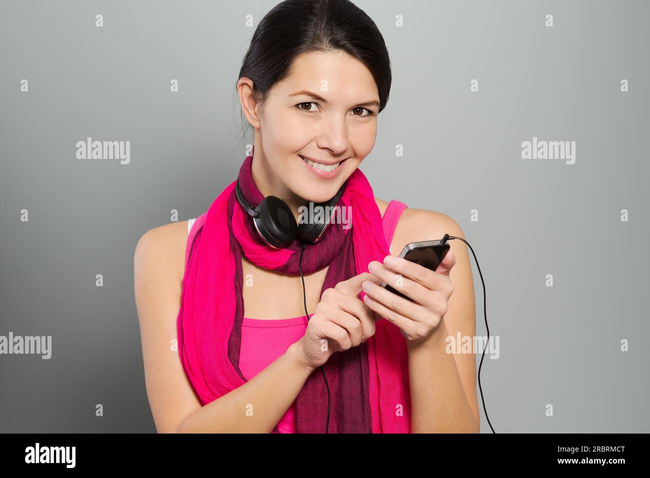 Bella donna sorridente che ascolta la musica in piedi con le cuffie intorno al collo mentre controlla i brani scaricati sul suo palmare portatile Foto Stock