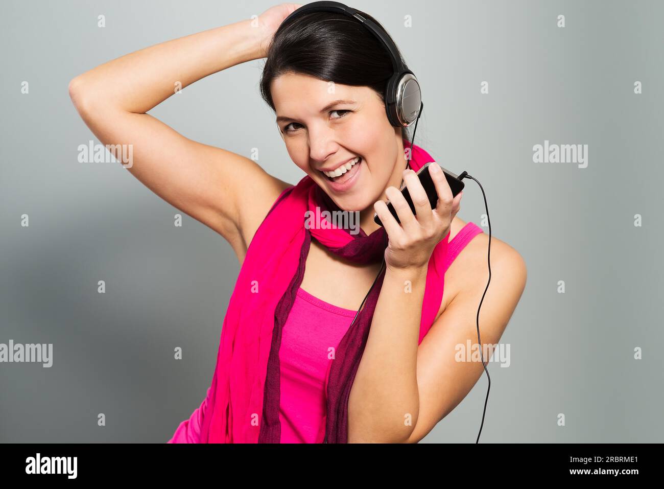 Bella donna vivace ascoltando musica su cuffie collegate al dispositivo elettronico del dispositivo di memorizzazione come essa si erge ridere per la fotocamera Foto Stock