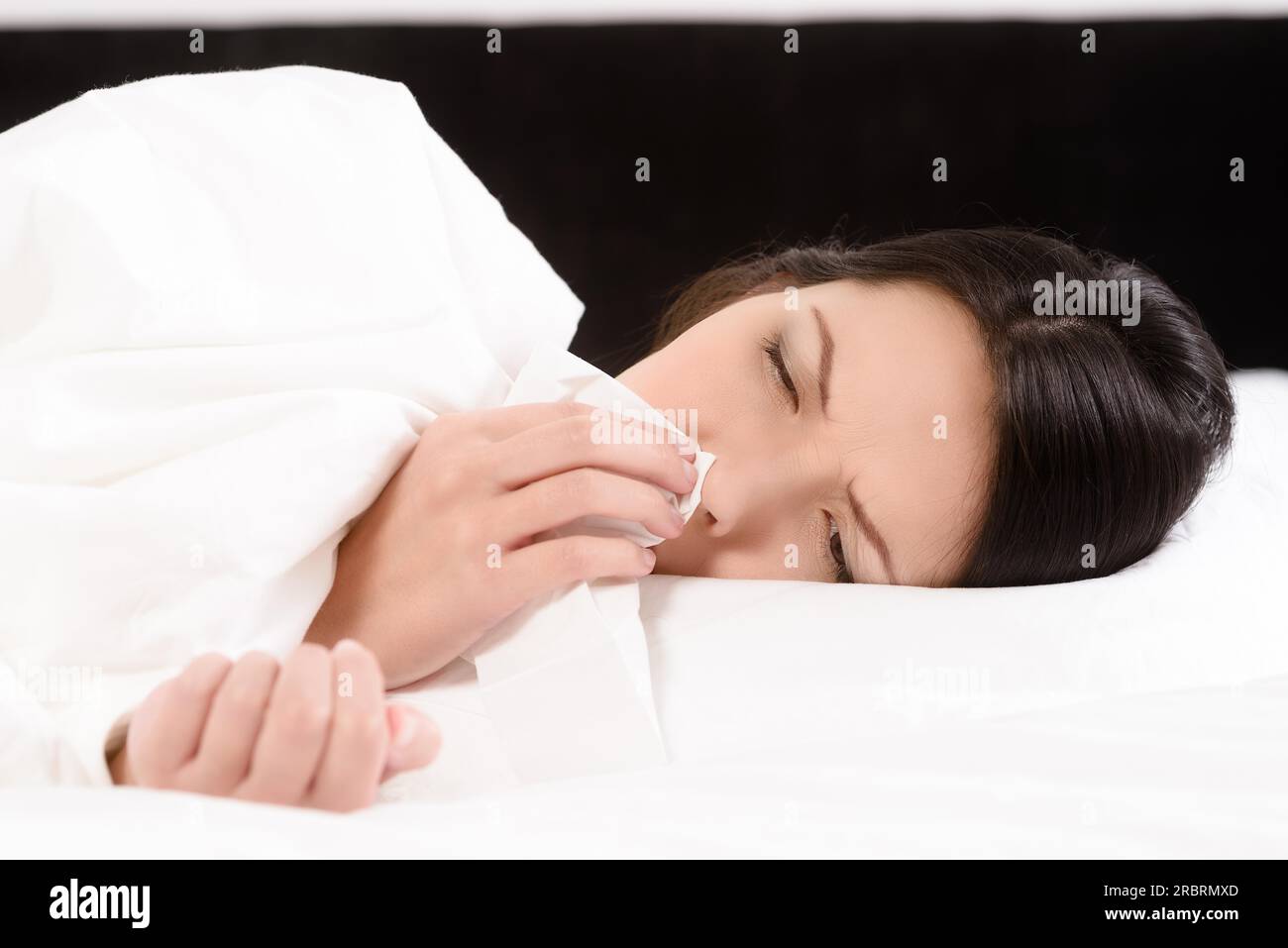 Giovane donna malata sdraiata nel suo letto bianco pulito soffiando il naso su un tessuto concettuale di assistenza sanitaria e influenza stagionale e brividi, rinite o un Foto Stock