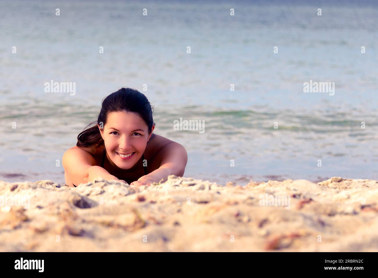 Sorridenti bella giovane donna body surf in su una piccola onda al mare come ella gode di un estate tropicale vacanza al mare Foto Stock