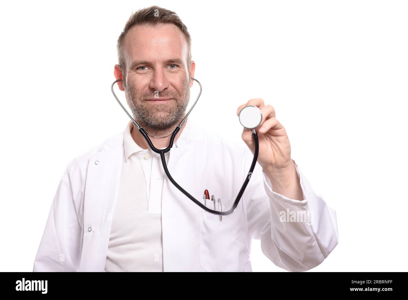 Medico maschio sorridente e non rasato che tiene in mano il disco di uno stetoscopio pronto a fare un esame mentre guarda la telecamera, isolato Foto Stock