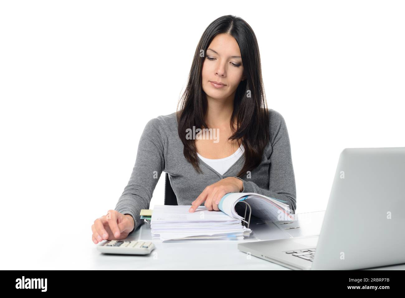Giovane donna che controlla un rapporto o le fatture in un raccoglitore di grandi dimensioni, che esegue calcoli manuali per verificare le cifre su una calcolatrice da tavolo Foto Stock