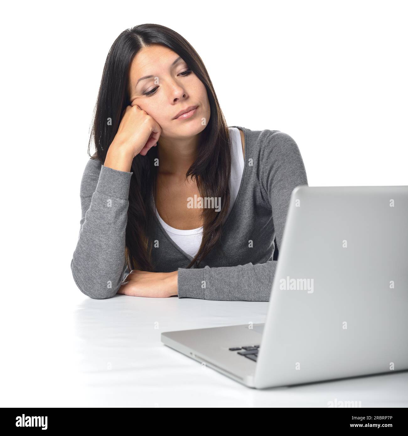 Donna d'affari annoiata seduta alla sua scrivania con la testa appoggiata al pugno che fissa il suo computer portatile con un'espressione rassegnata, sul bianco Foto Stock