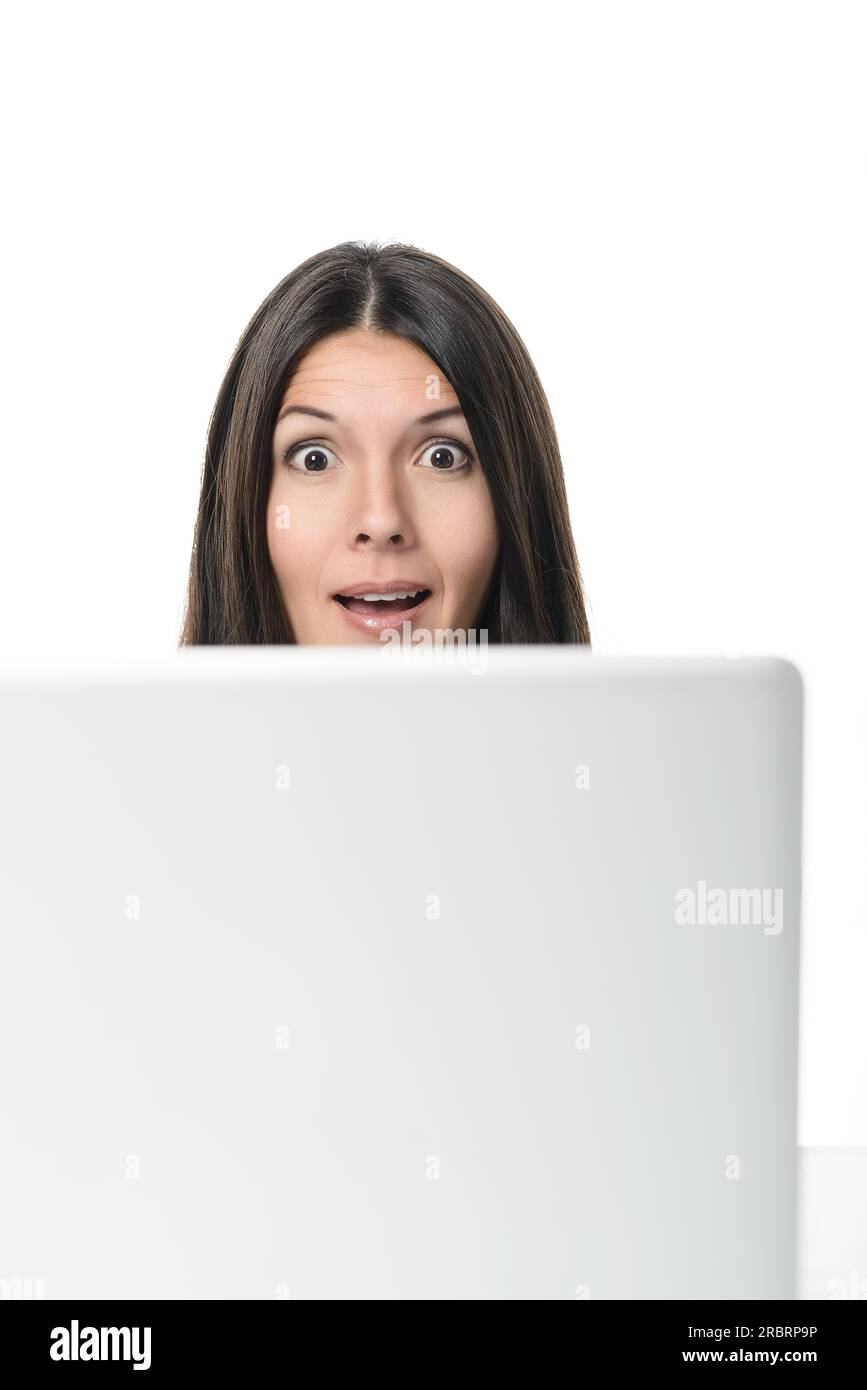 Donna d'affari che guarda la fotocamera dalla parte superiore dello schermo del suo computer con uno sguardo di sorpresa, shock, stupore e ammirazione con la bocca aperta Foto Stock