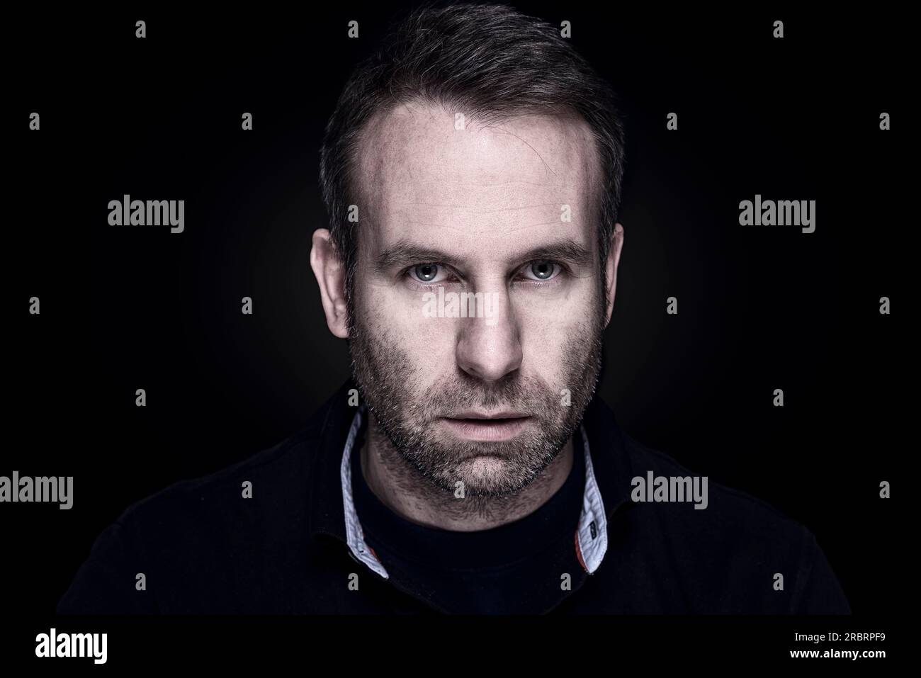 Bello e sfacciato uomo di mezza età con un'espressione cupa e seria che guarda direttamente la fotocamera, la testa scura e lunatica e il ritratto delle spalle Foto Stock