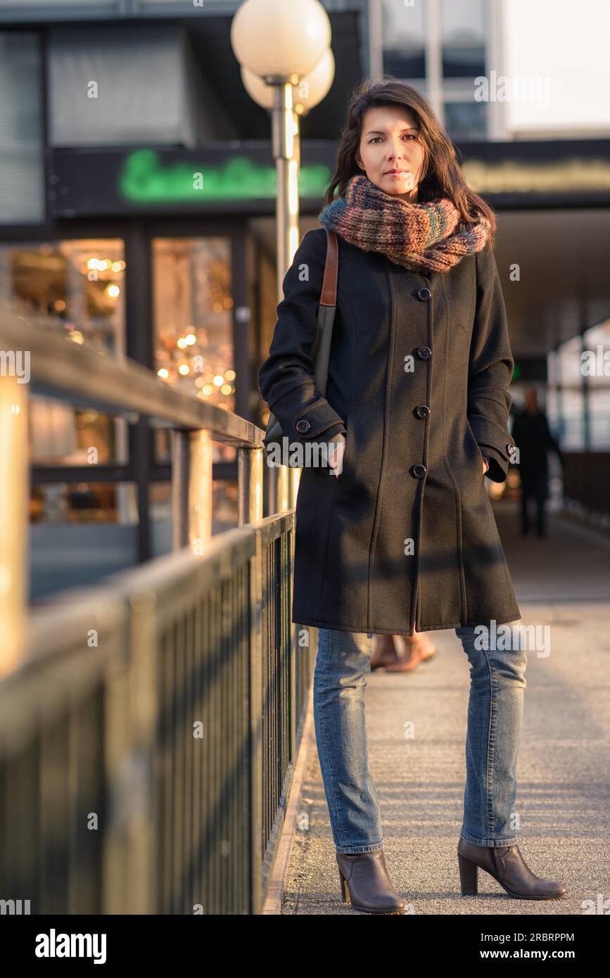 Foto a lunghezza intera di elegante Pretty Young Woman in autunno, che si appoggia sulle guide laterali del vialetto e guarda la fotocamera Foto Stock