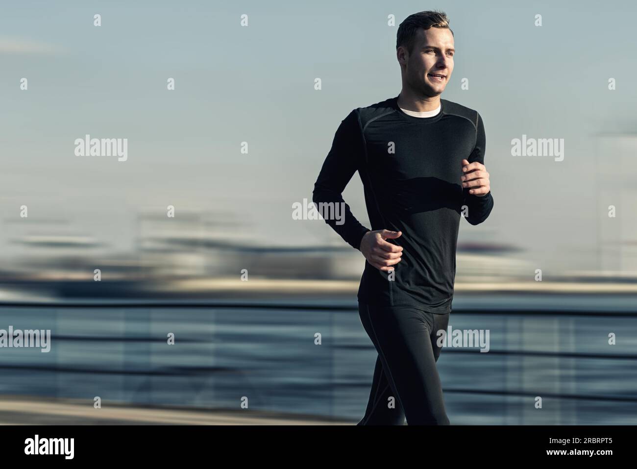 Abbigliamento atletico e bello Man in Black Workout che corre al River Bridge la mattina presto Foto Stock