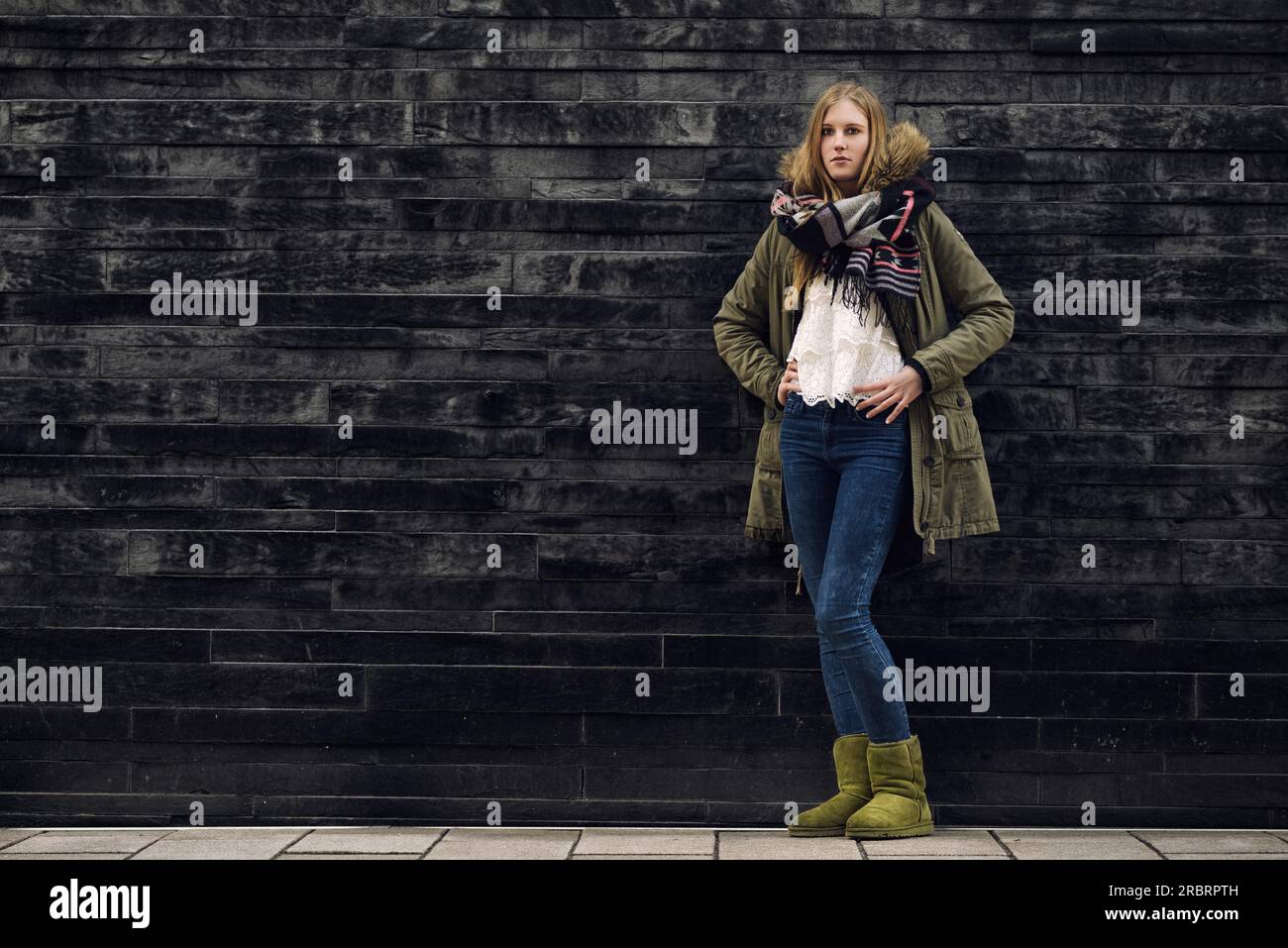 Giovane donna alla moda in abito invernale in posa davanti alla vecchia parete grigia mentre guarda la fotocamera Foto Stock